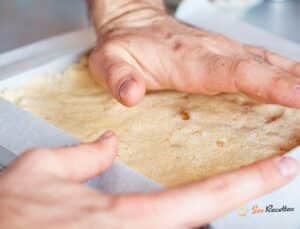 Carrés de shortbread macadamia sirop d'érable sur planche en bois avec papier parchemin et pot de maple syrup