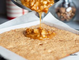 Caramel macadamia brillant versé depuis une casserole sur base shortbread dans cadre carré, vue de face