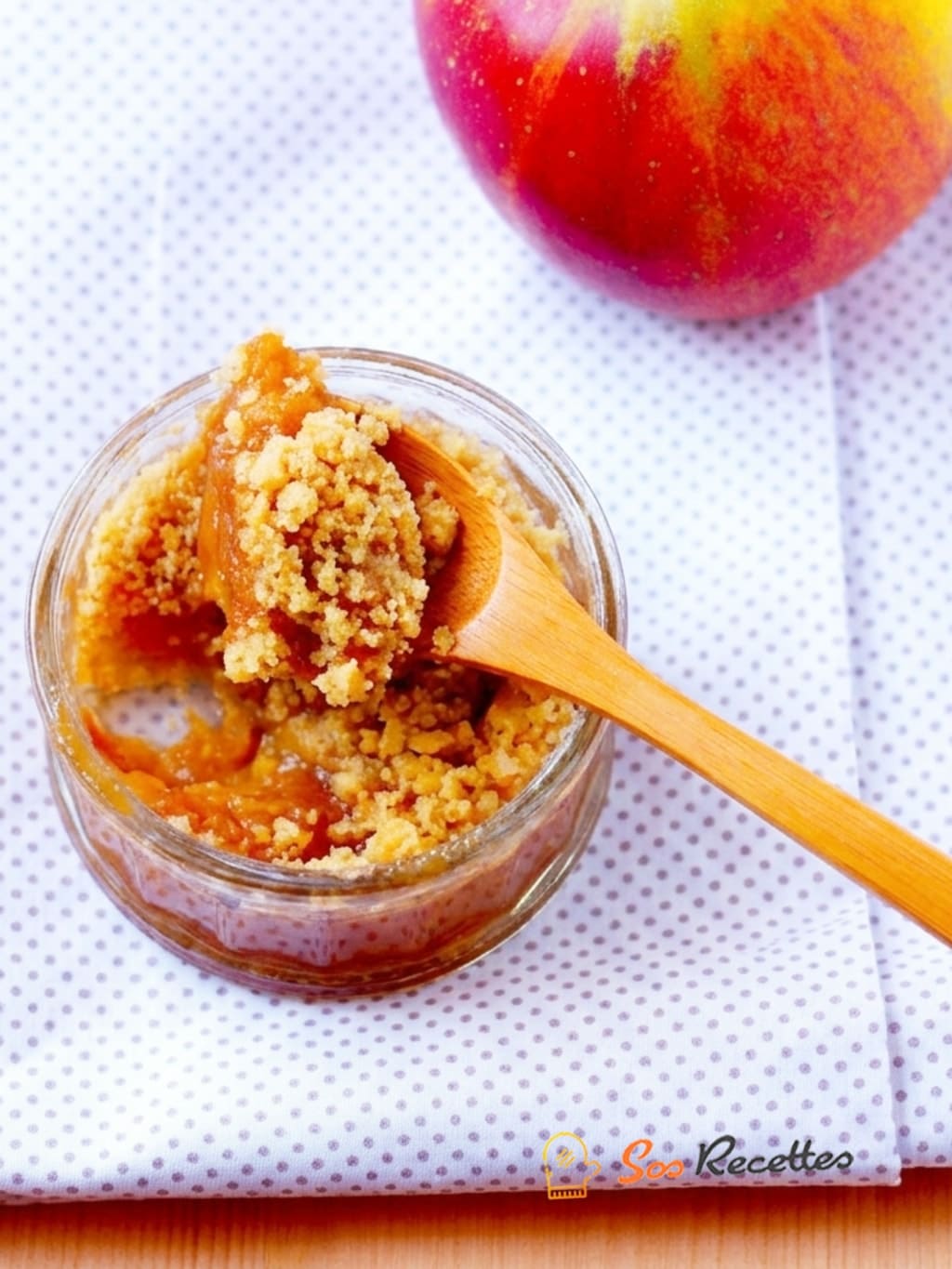 Crumble aux pommes maison dans un petit pot en verre avec une cuillère en bois et une pomme fraîche sur fond clair