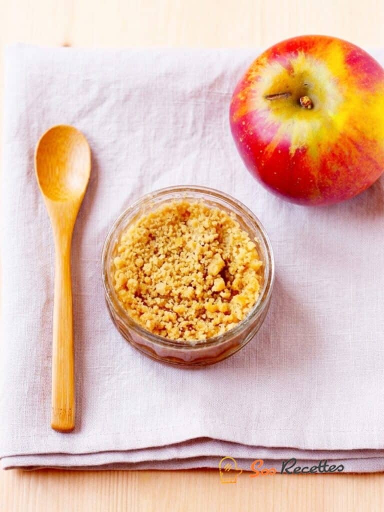 Crumble aux pommes croustillant servi en verrine avec topping doré et pomme rouge sur table en bois